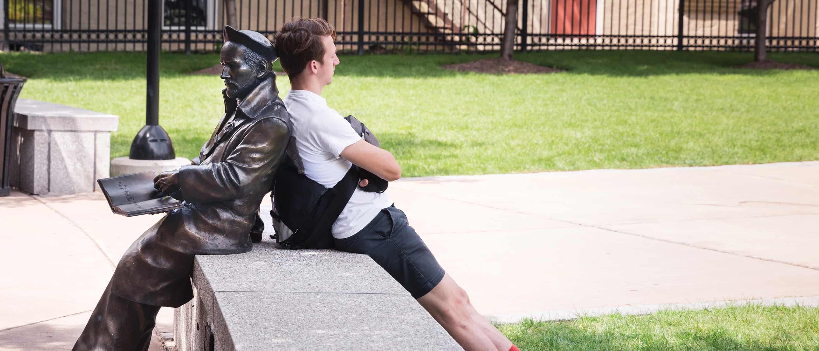 student relaxing in front of the MacMahon Center leaning against the stature of Saint Ignatius Loyola