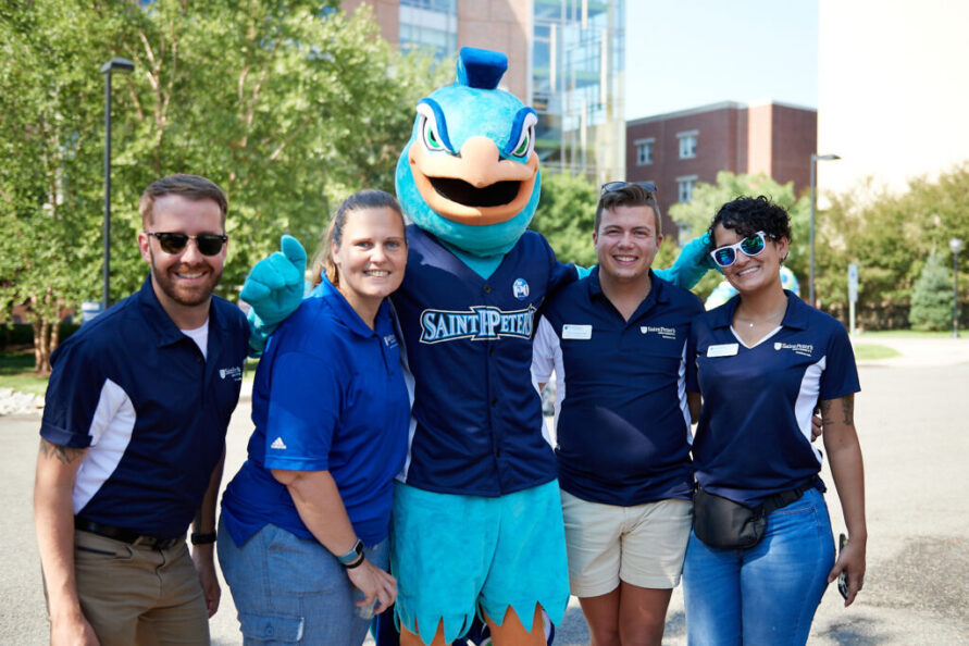 Image of four individuals smiling with the peacock mascot.