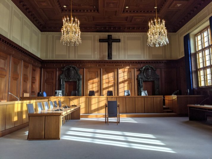 A courtroom at Nuremberg, Germany. The room is empty and sunlight streams in from the large windows on the right.